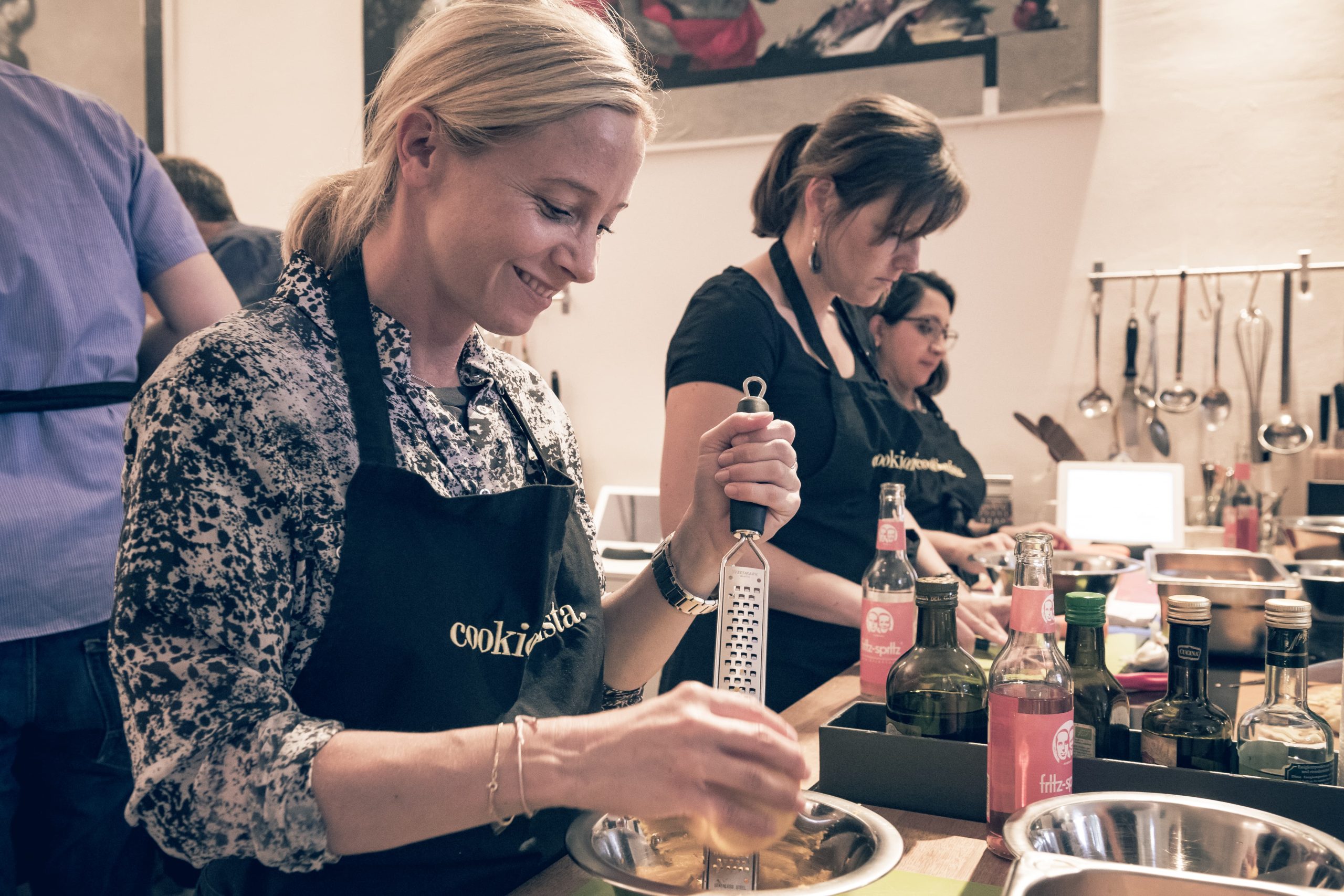 Teilnehmerin eines Junggesellenabschieds beim Kochkurs, lachend und konzentriert mit einer Reibe in der Hand