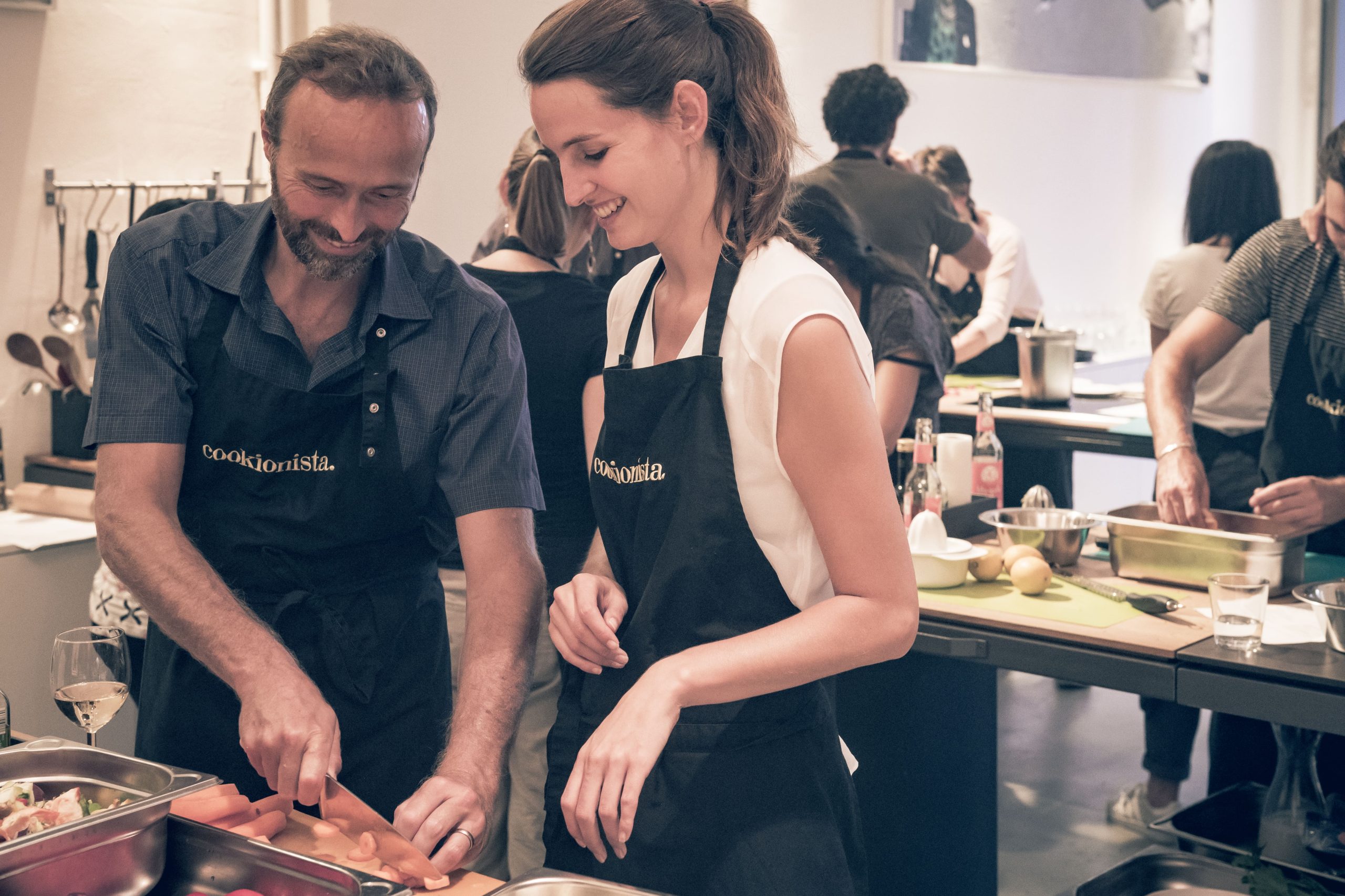 Paar kocht zum Valentinstag gemeinsam in einem Kochkurs, lachend und konzentriert an einer Kochstation