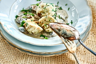 Semmelkloß mit Pilzrahmsoße und Petersilie auf einem weißen Teller mit Besteck